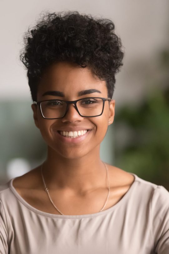 Head shot portrait of happy mixed race girl wearing glasses, smiling african american millennial woman posing indoor, pretty positive female student businesswoman young professional looking at camera